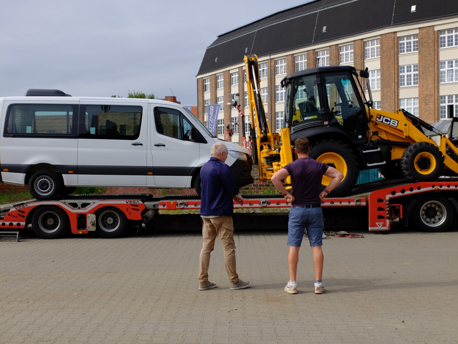 ein Sprinter Kastenwagen mit Rollrampe und ein Multifunktionsradlader stehen auf einem Auflieger von einem LKW
