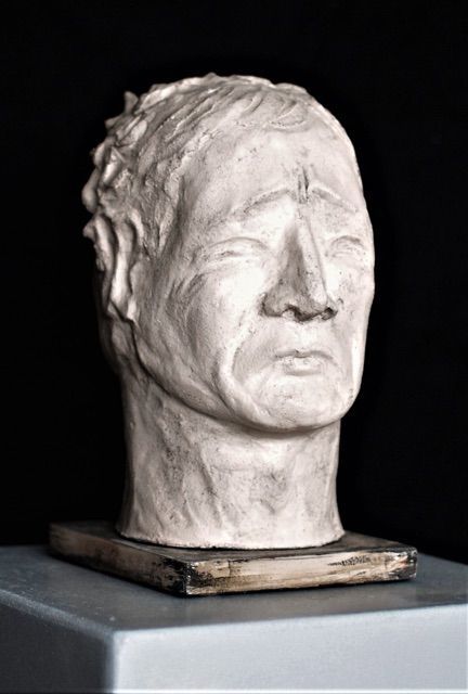 Die eine Seite der Skulptur zeigt ein lachendes, die andere ein trauriges Gesicht. Die Skulptur besteht aus gebranntem weißem Ton.