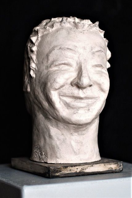 Die eine Seite der Skulptur zeigt ein lachendes, die andere ein trauriges Gesicht. Die Skulptur besteht aus gebranntem weißem Ton.