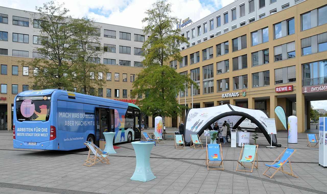 #MachsMitUns - Mobile Berufsberatung des Bezirksamts Marzahn-Hellersdorf auf dem Alice-Salomon-Platz - Übersicht über den Informationsstand mit dem Kampagnen-Bus "Machs-mit-uns" der Berliner Senatsverwaltung, dem Pavillion des Bezirksamts und verschiedenen Werbematerialien auf dem Alice-Salomon-Platz unter dem Schriftzug "Rathaus"