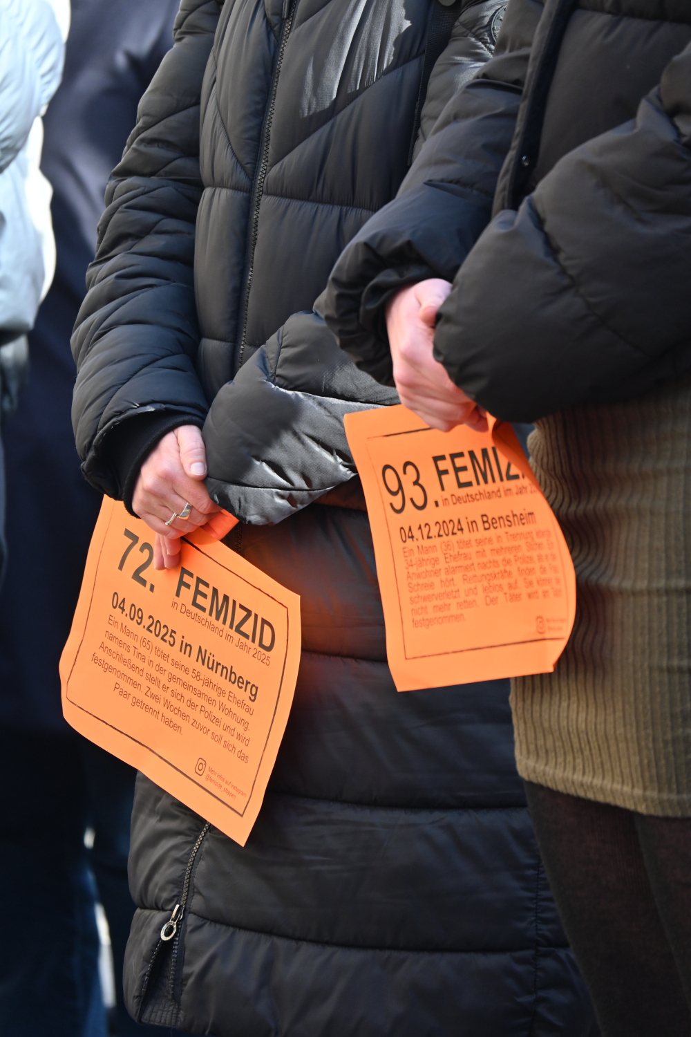 Zwei orangene Schilder mit Femiziden aus Deutschland werden gehalten.
