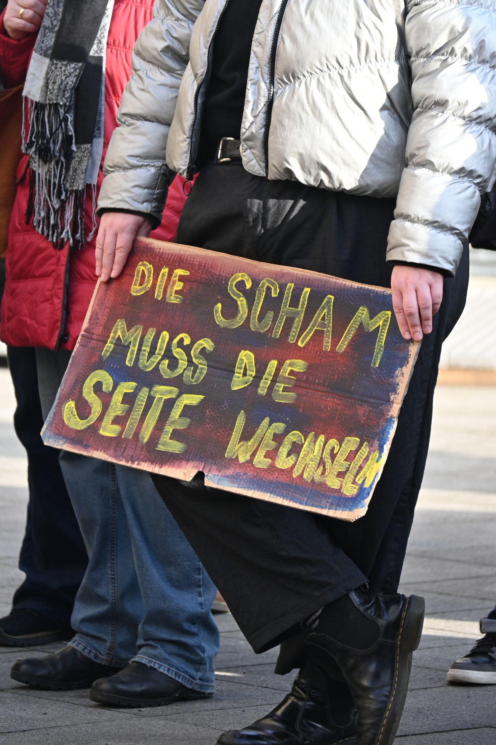 Ein Demoschild mit dem Text "Die Scham muss die Seite wechseln" wird gehalten.