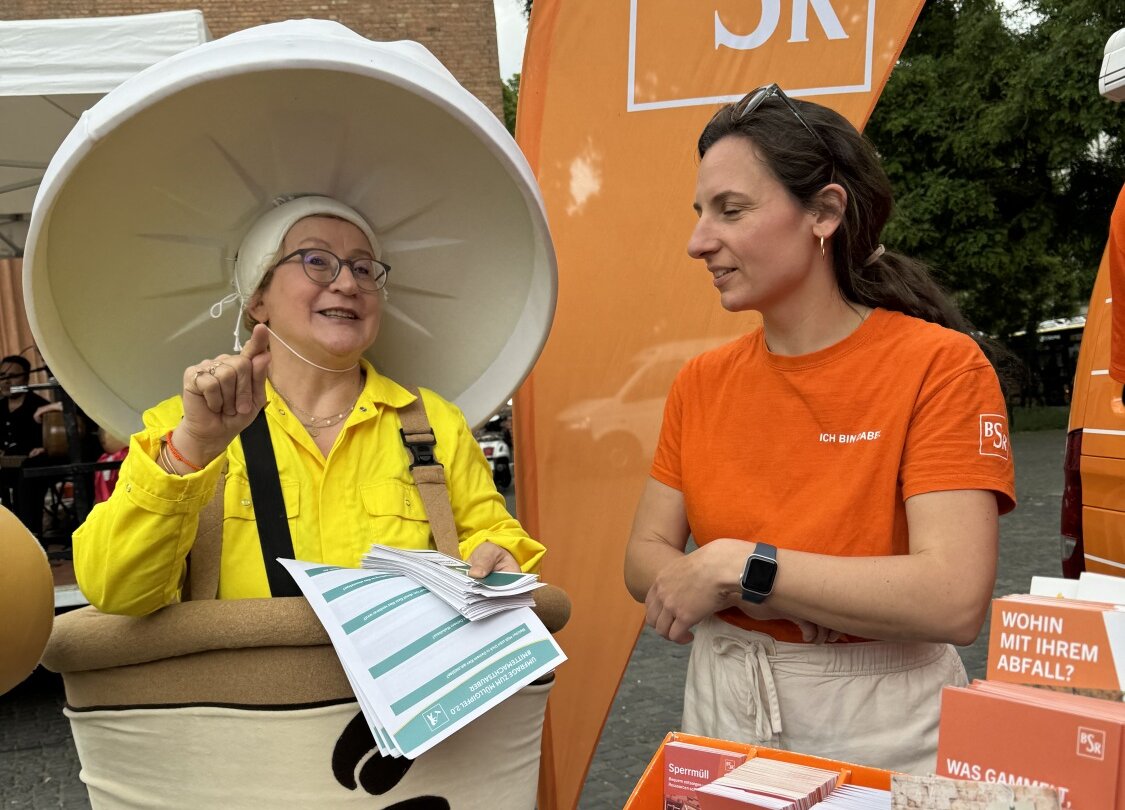 Mitarbeiterin von Life e.V. im Müllkostüm im Gespräch mit Mitarbeiterin der BSR