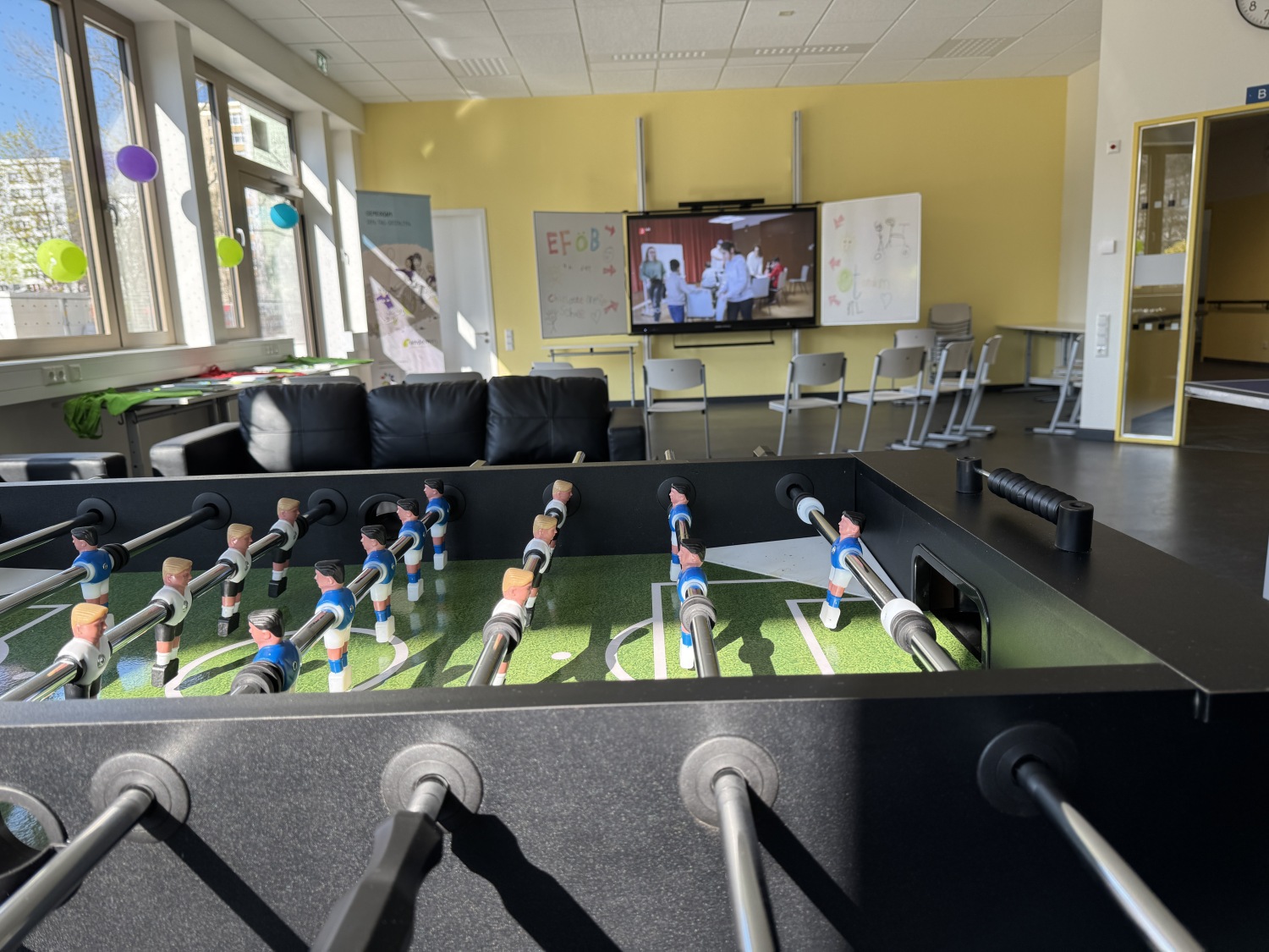 Gemeinschaftsraum des modularen Ergänzungsbaus mit Tischkicker und Leinwand.