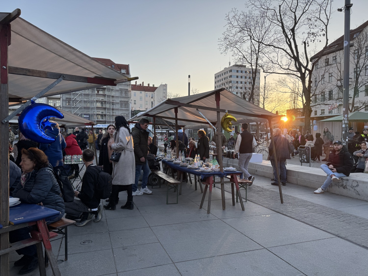Menschen sitzen beim gemeinsamen Fastenbrechen auf Bänken am Leopoldplatz zusammen.