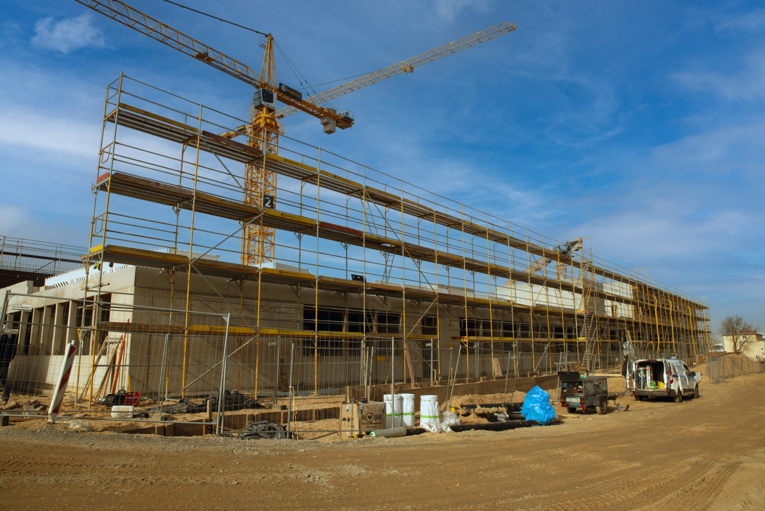 Ein Kran steht vor dem Baugerüst in dem bereits das EG auf der Baustelle der Clay-Schule in Neukölln