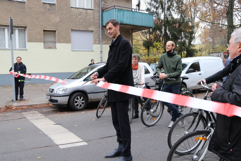 Bezirksbürgermeister Hikel schneidet das symbolische Band durch und übergibt die Fahrradstraße Weigandufer der Öffentlichkeit