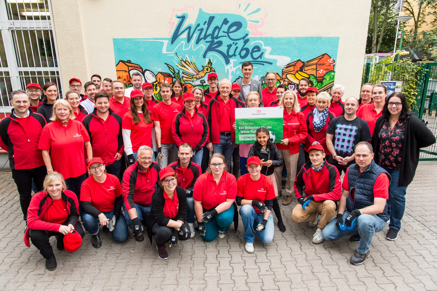 Ein Gruppenfoto von ungefähr 30 Personen in roten T-Shirts vor einem Wandbild mit dem Schriftzug Wilde Rübe