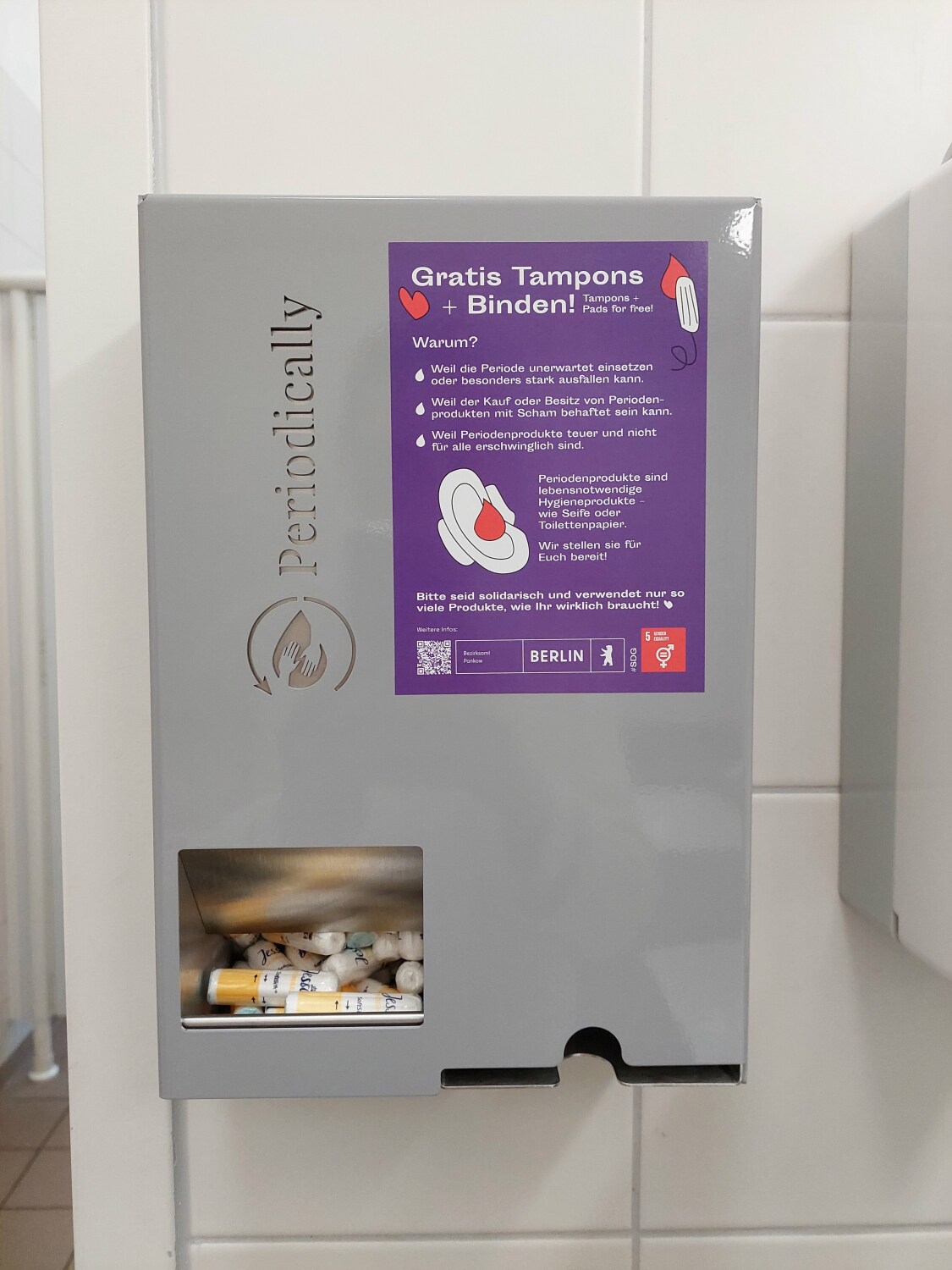 Ein Menstruationsartikelspender mit einem Informationsaufkleber in einem Toiletten-Raum