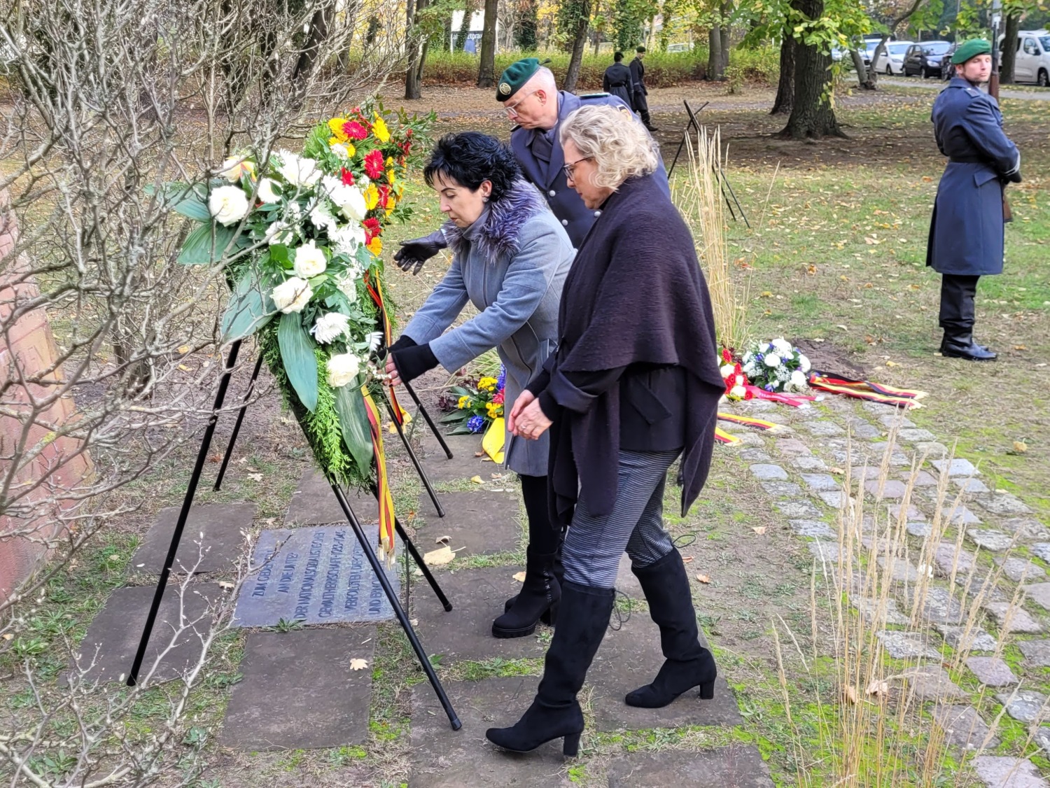 Bezirksbürgermeisterin Demirbüken-Wegner, BVV-Vorstandsmitglied Skrobek-Angerer (vorn) und der Kommandeur Landeskommando Berlin, Oberst Busch beim Richten der Kranzschleifen.busch