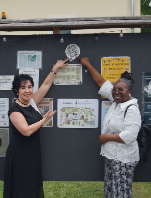 Bezirksbürgermeisterin Emine Demirbüken-Wegner (CDU) und Grace Adenmosun (GeTu Prospects e.V.) bringen den Sticker mit dem Logo für Einsamkeit an der alten Fasanerie an