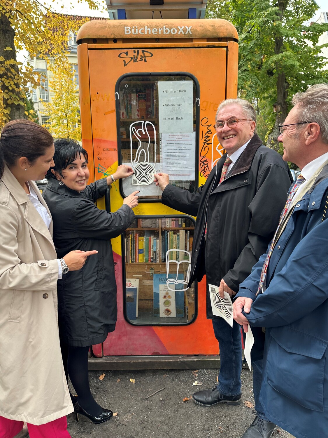 v.l.: Einsamkeits- und Ehrenamtsbeauftragte Katharina Schulz, Bezirksbürgermeisterin Emine Demirbüken-Wegner, Bernd Roske vom Verein „Energie für Bildung“ und Hans-Dieter Pohl bringen den Sticker gegen Einsamkeit an der BücherboXX an