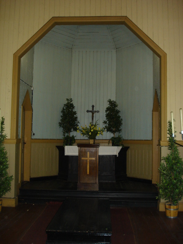 Ansicht des Altarbereichs der Feierhalle Staaken, weiß-beige Holzvertäfelung, Altar mit Kreuz und Pflanzen