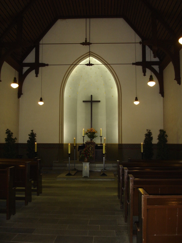 Ansicht des Altarbereichs der Feierhalle Kisseln, Altar mit Kreuz, Kerzen und Pflanzen, davor Sitzreihen