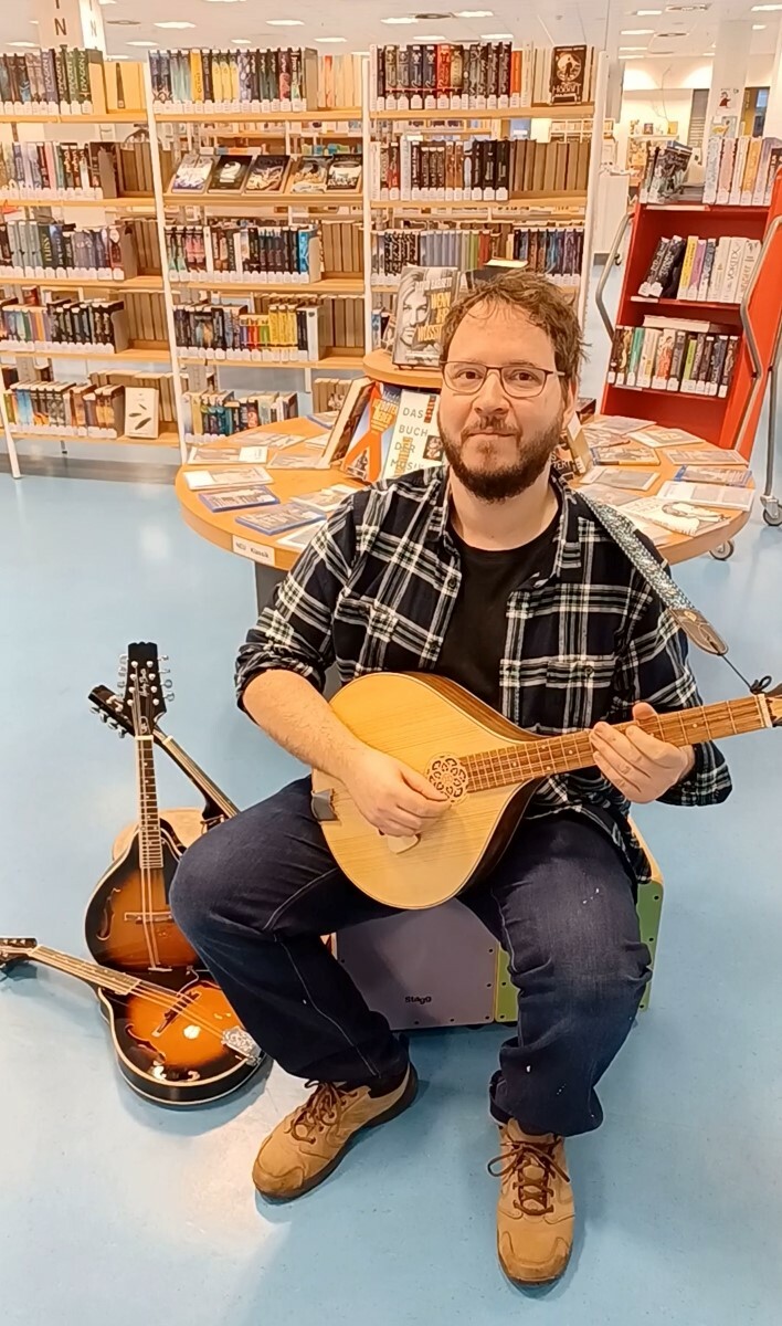 Ein Mitarbeiter der Stadtbibliothek mit einer Mandoline in der Ingeborg-Drewitz-Bibliothek