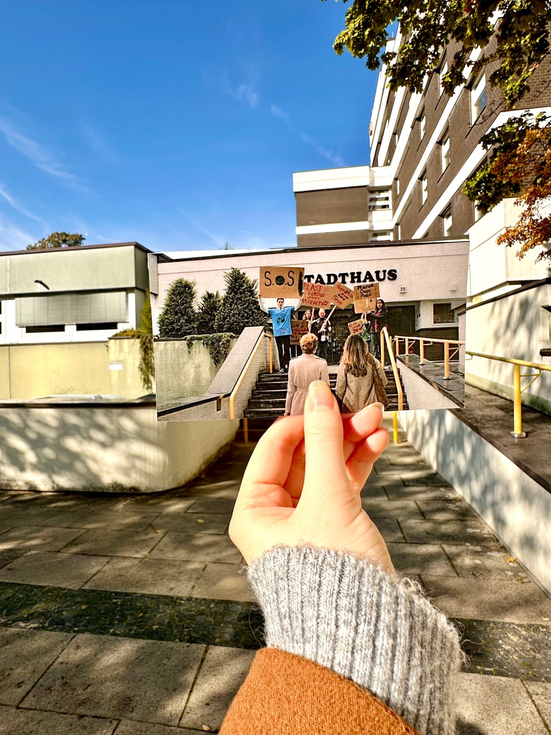 Hand hält Foto einer Filmszene mit mehreren Personen die Richtung Haupteingang blicken