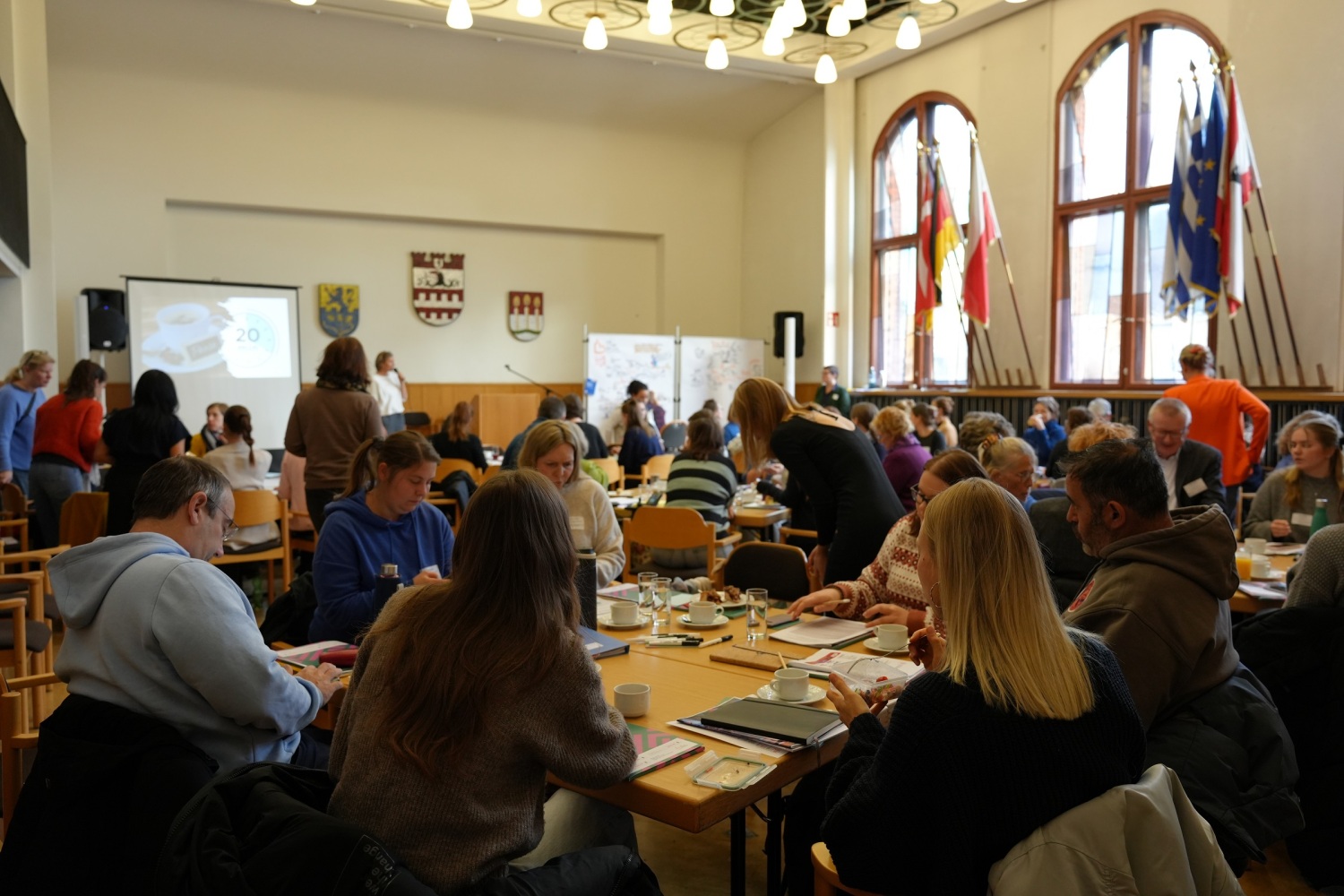 Blick in den Saal mit vielen Teilnehmenden an einzelnen Gruppentischen
