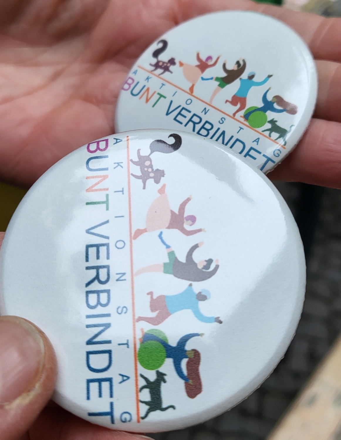 DIY-Buttons mit dem Logo Aktionstag BUNT VERBINDET: 2 fertige Buttons auf der Hand