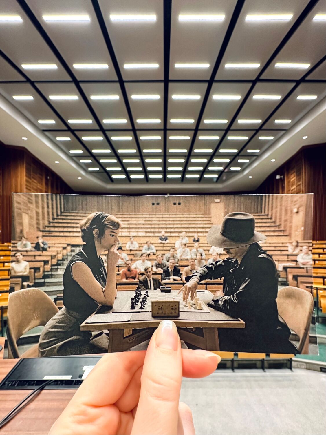 Hand hält Foto einer Filmszene mit zwei Personen (Anya Taylor-Joy & Thomas Brodie-Sangster) in die Kulisse des Drehorts