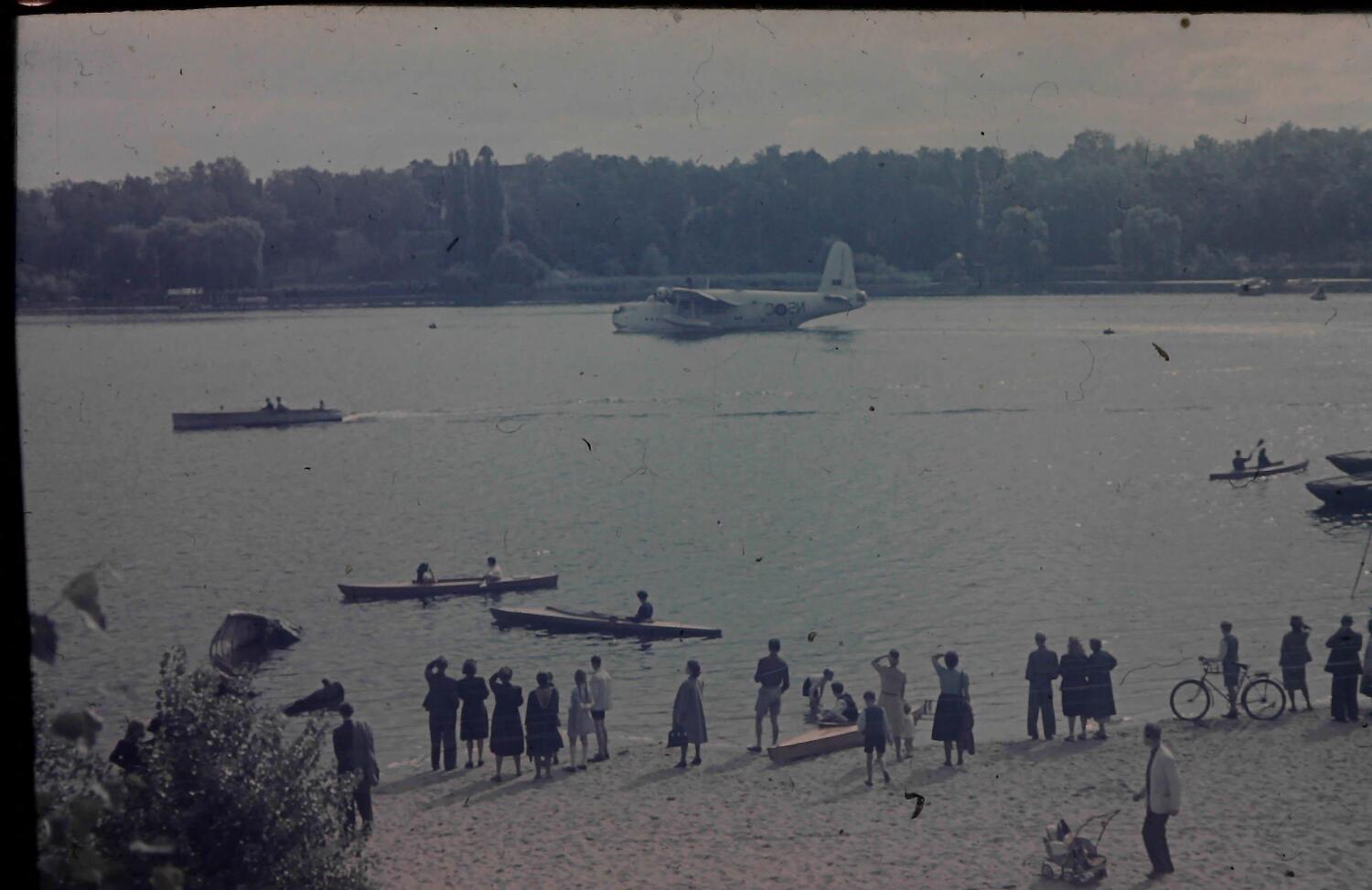 Ein altes Foto von einem Gewässer. Am Ufer stehen Menschen und schauen aufs Wasser zu einem Wasserflugzeug.