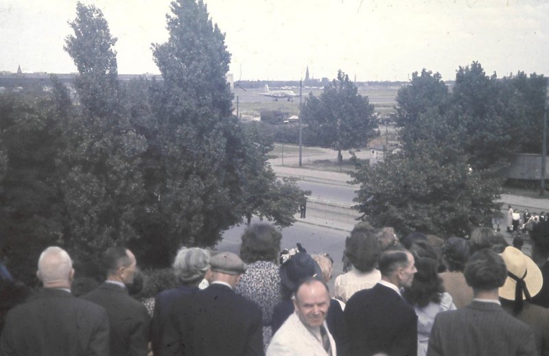Ein altes Foto von Menschen, die auf einen Flugplatz mit einem Flugzeug schauen.