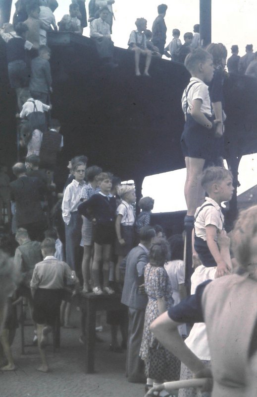 Menschen, insbesondere viele Kinder, stehen auf Podesten und Erhöhungen und schauen in die Ferne.