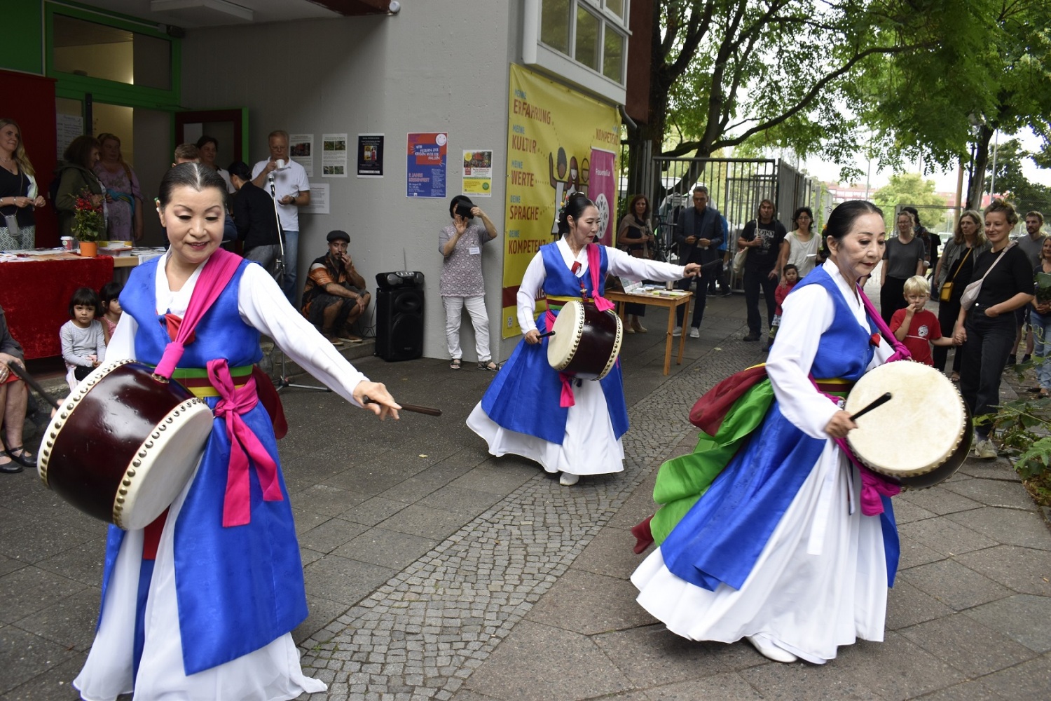 Drei Frauen in traditioneller koreanischer Kleidung trommeln und tanzen.