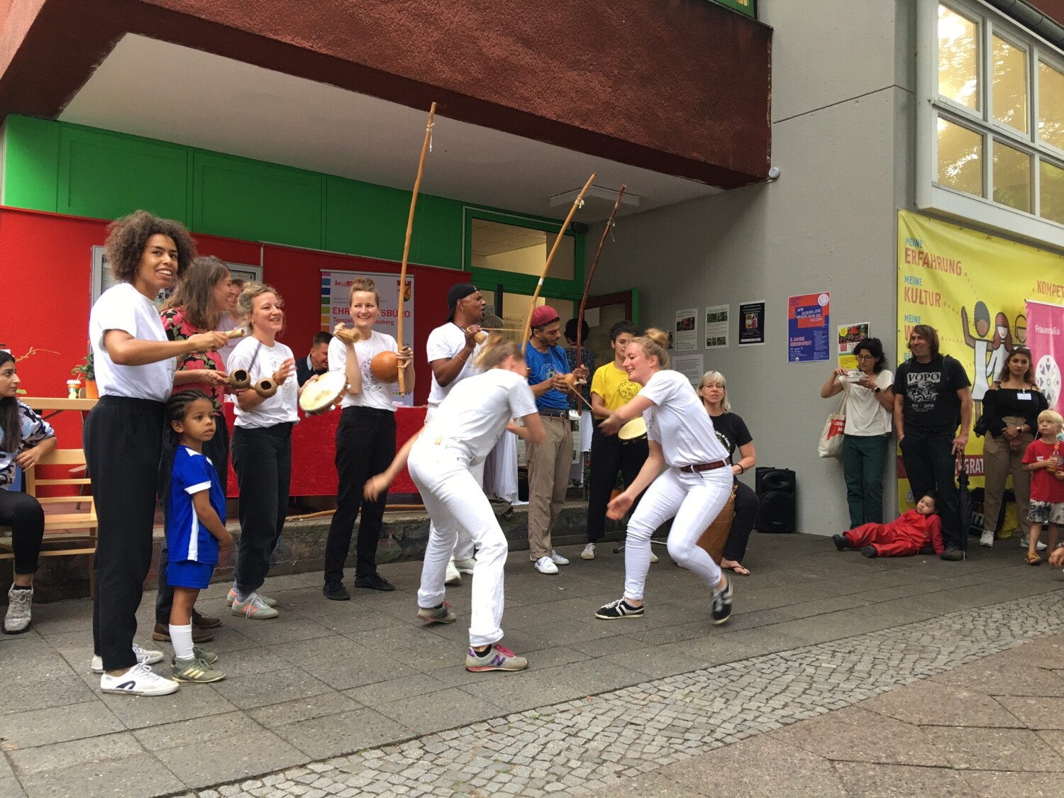 Zwei Frauen stehen sich gegenüber und führen etwas vor. Rundherum stehen Menschen.