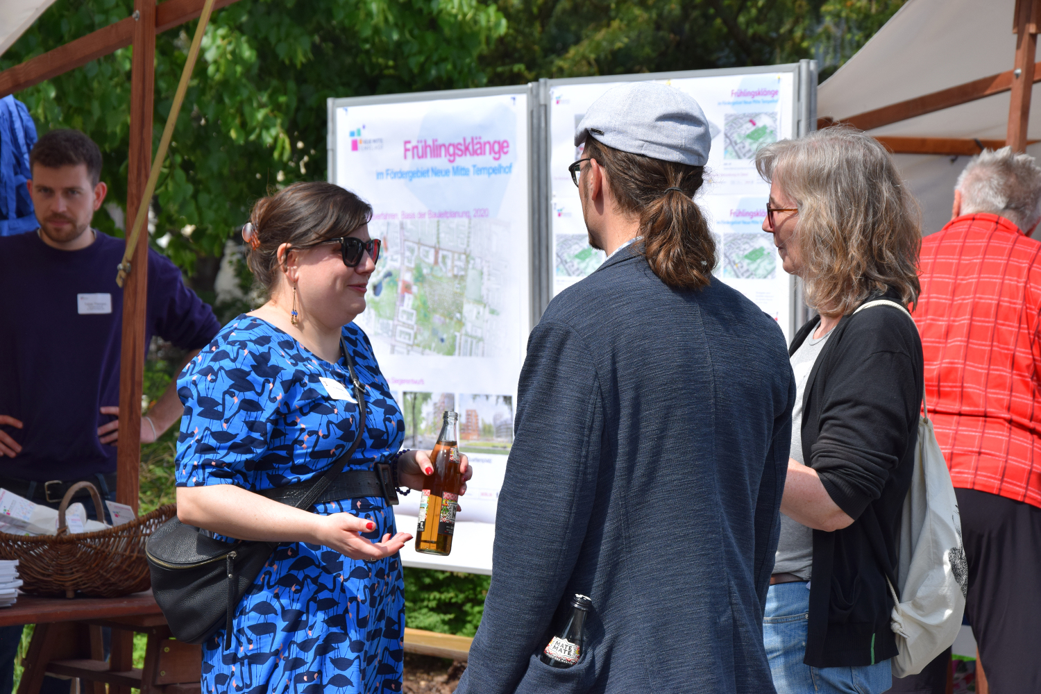 Drei Personen unterhalten sich. Im Hintergrund sind Informationstafeln und Stände.