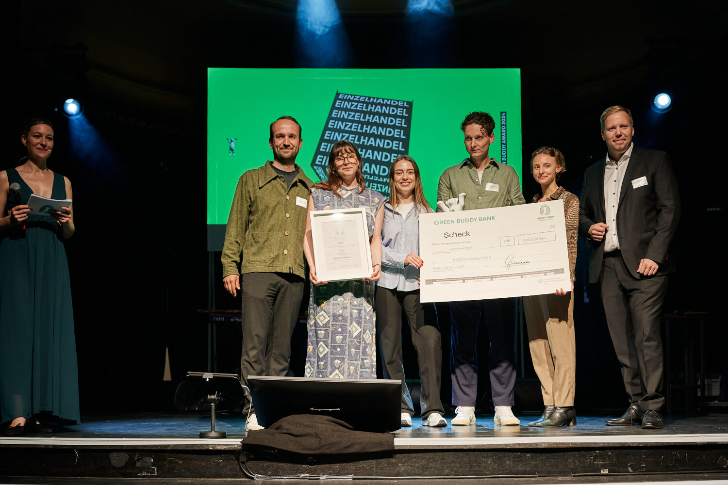 Auf einer Bühne stehen Personen zusammen und halten eine Bären-Statue, eine Urkunde und einen Scheck in den Händen.