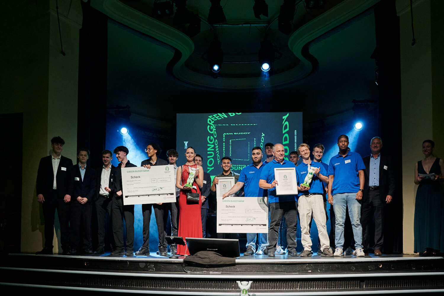 Auf einer Bühne stehen Personen zusammen und halten eine Bären-Statue, eine Urkunde und einen Scheck in den Händen.