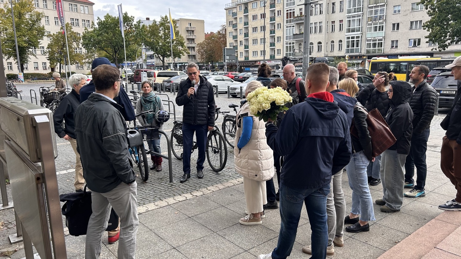 Eine Gruppe Menschen steht draußen zusammen und eine Person spricht etwas in ein Mikrofon.