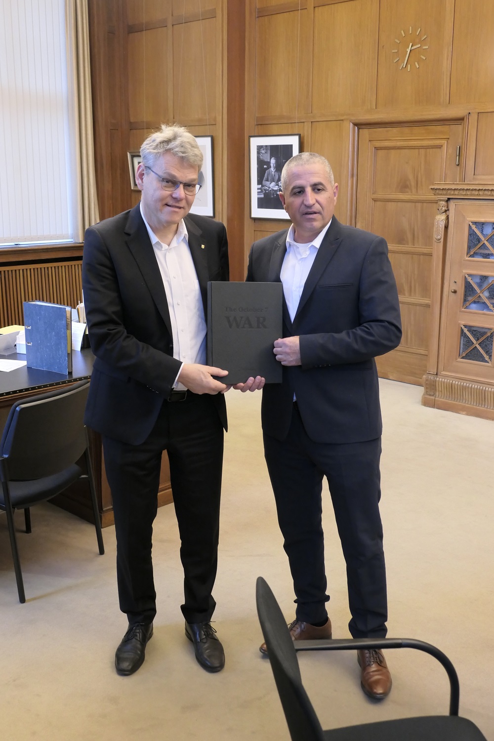 Zwei Männer halten ein schwarzes Buch in den Händen, auf dem W A R steht