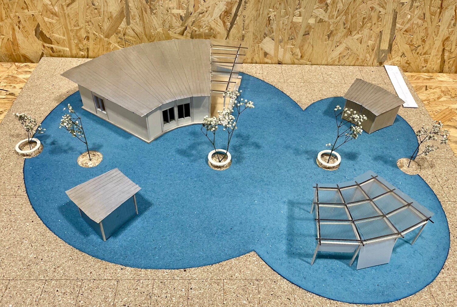 Modell eines Platzes aus Holz. Verschiedene Gebäude und Pflanzen sind in einem durch Kreise angeordneten Platz aufgebaut.