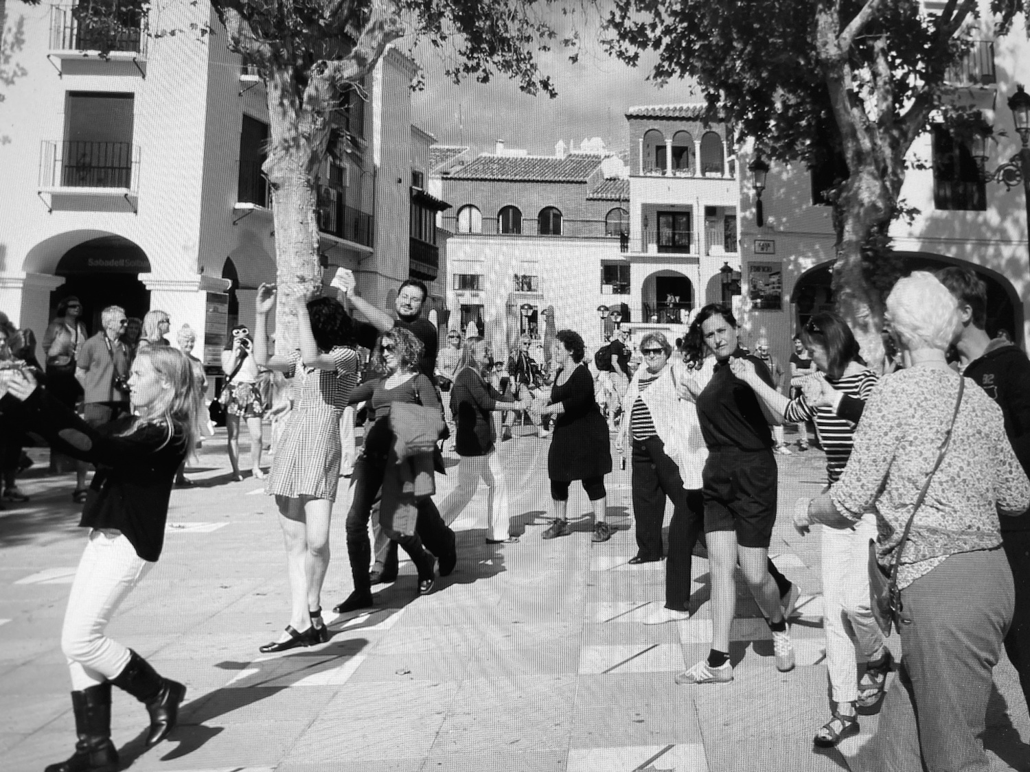 Schwarzweißfotografie von Menschen, die draußen auf einem Platz tanzen.