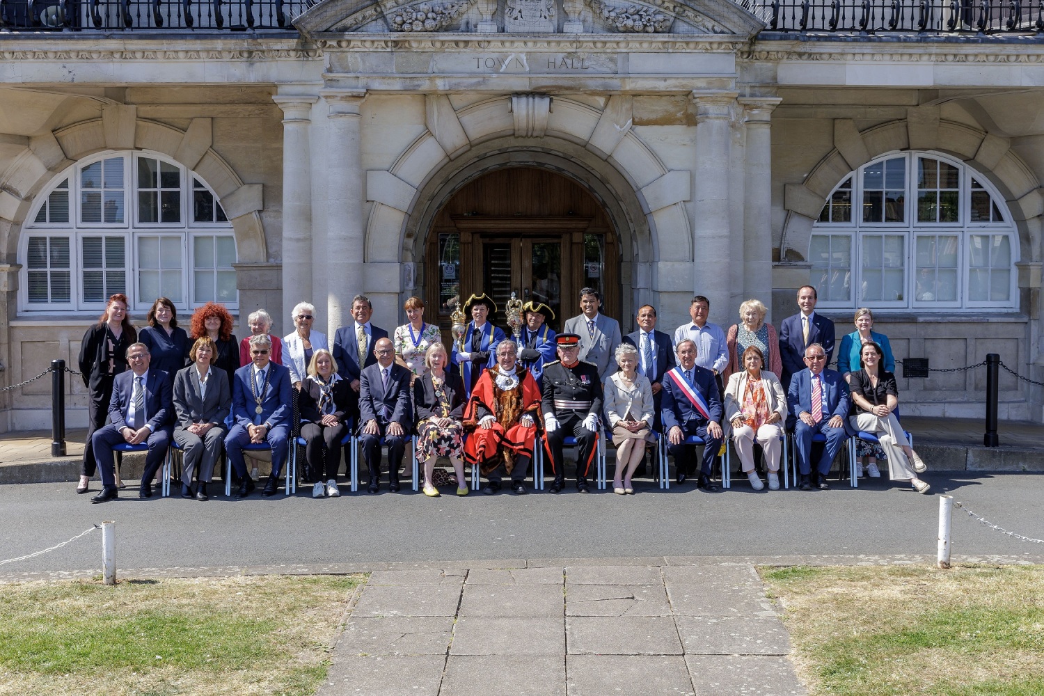 Ganze viele Menschen sitzen und stehen in zwei Reihen vor einem historischen Gebäude.