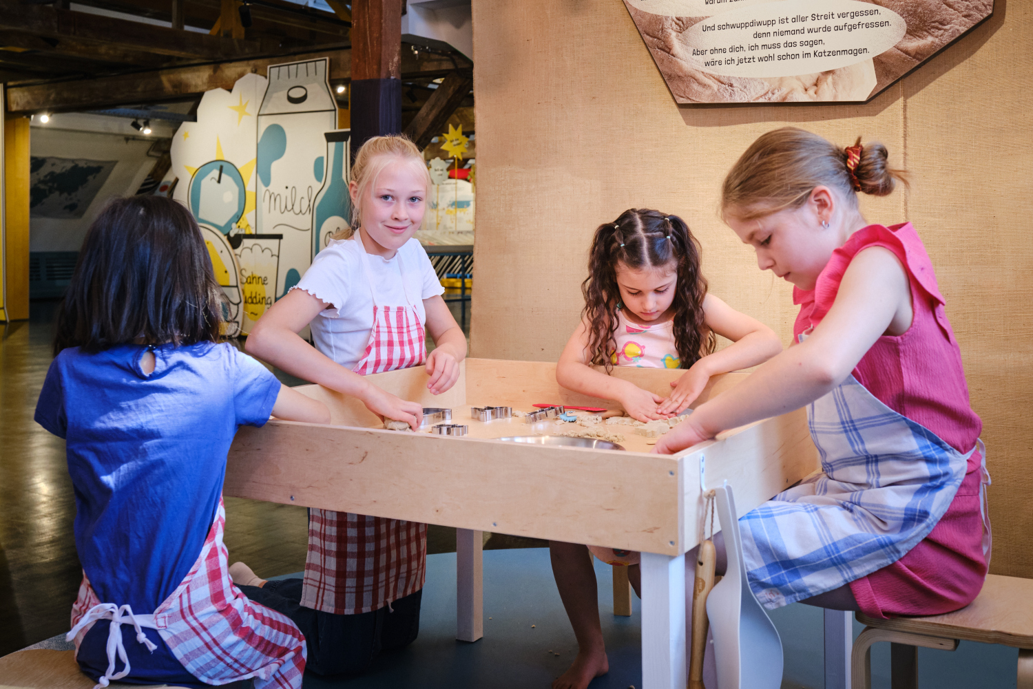 Vier Kinder mit Schürzen sitzen um einen Tisch und arbeiten mit Ausstechformen.