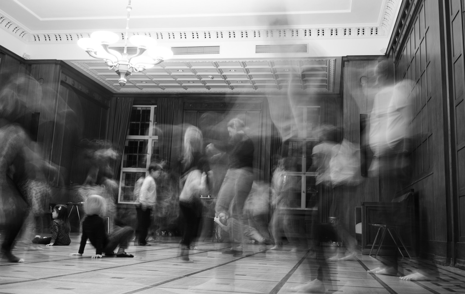 Schwarzweißfotografie von Menschen, die sich in einem Saal bewegen. Die genauen Umrisse sind unscharf.