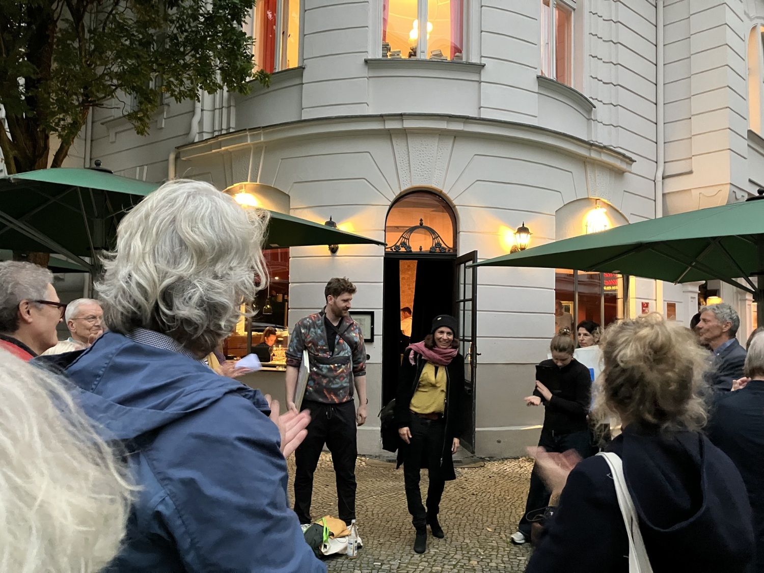 Zwei Personen stehen auf einem Gehweg und sprechen zu einer Menschenmenge.