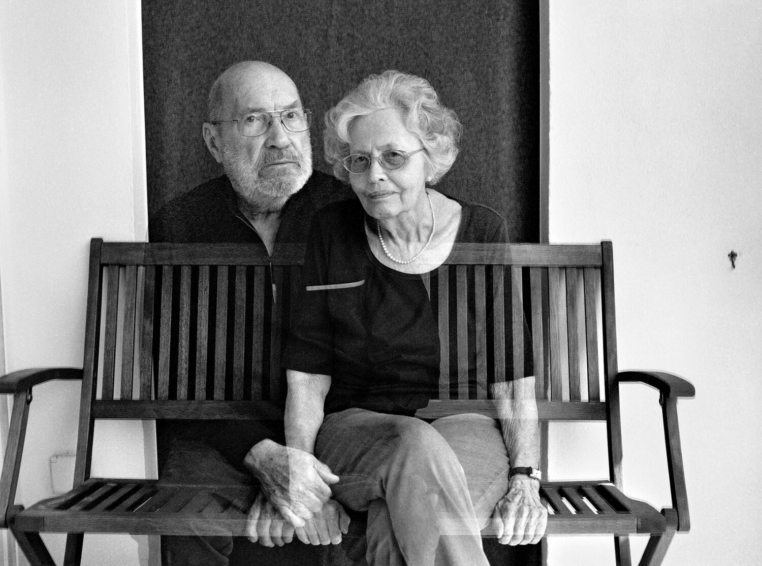 Schwarzweißfotografie; zwei Menschen sitzen auf einer Bank, aber sie sind leicht transparent.