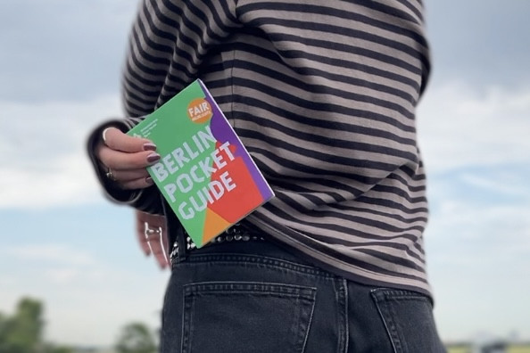 Eine Person zieht eine kleine Broschüre aus der Hosentasche.