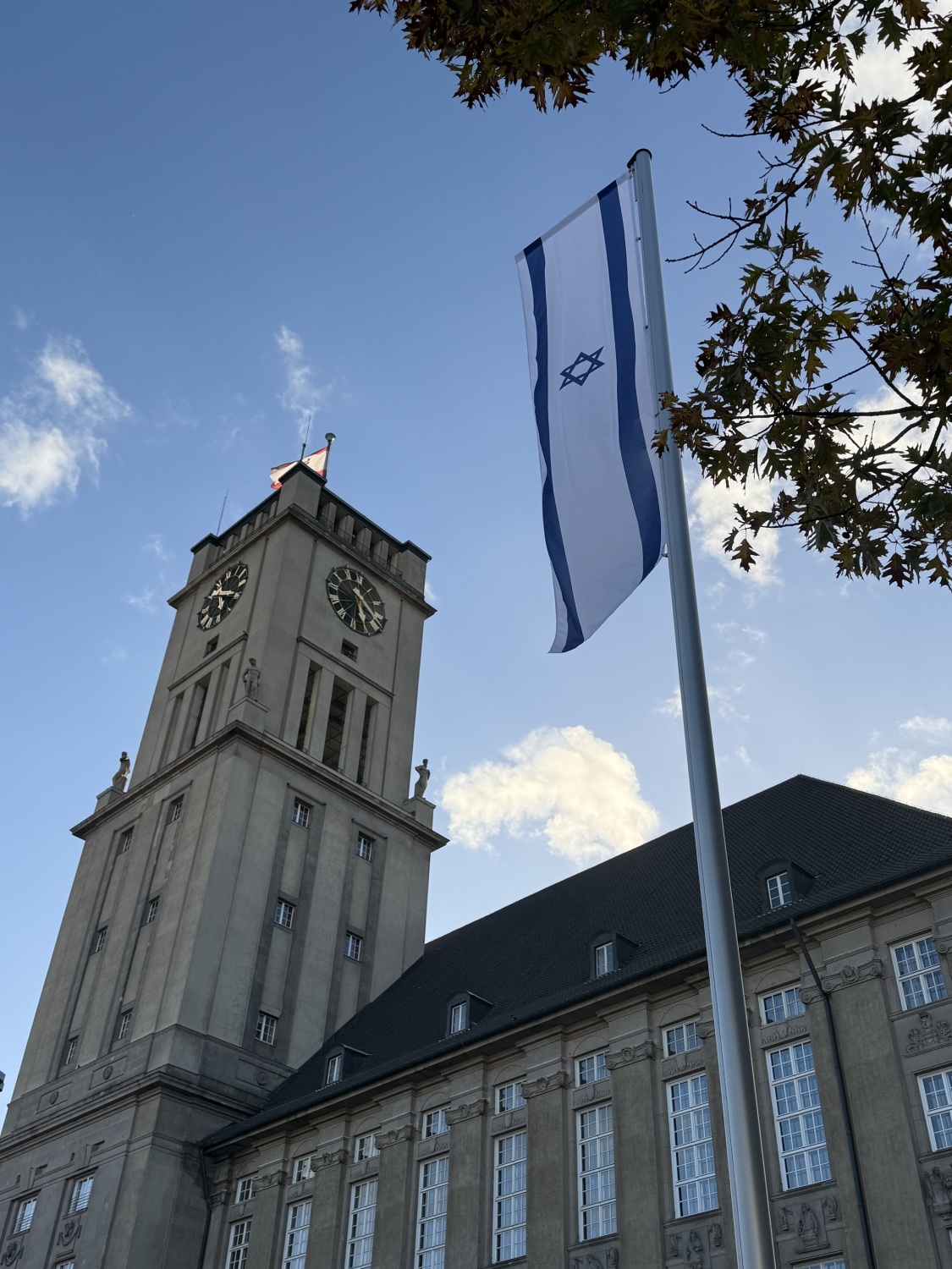 Vor einem großen Gebäude mit Uhrenturm weht an einem Fahnenmast die israelische Flagge.