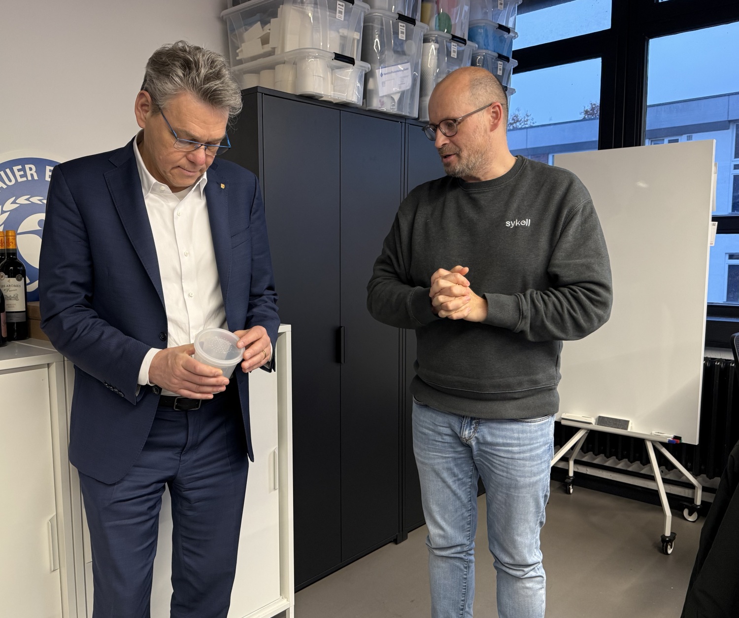 Zwei Männer stehen in einem Büro und schauen auf eine Verpackung