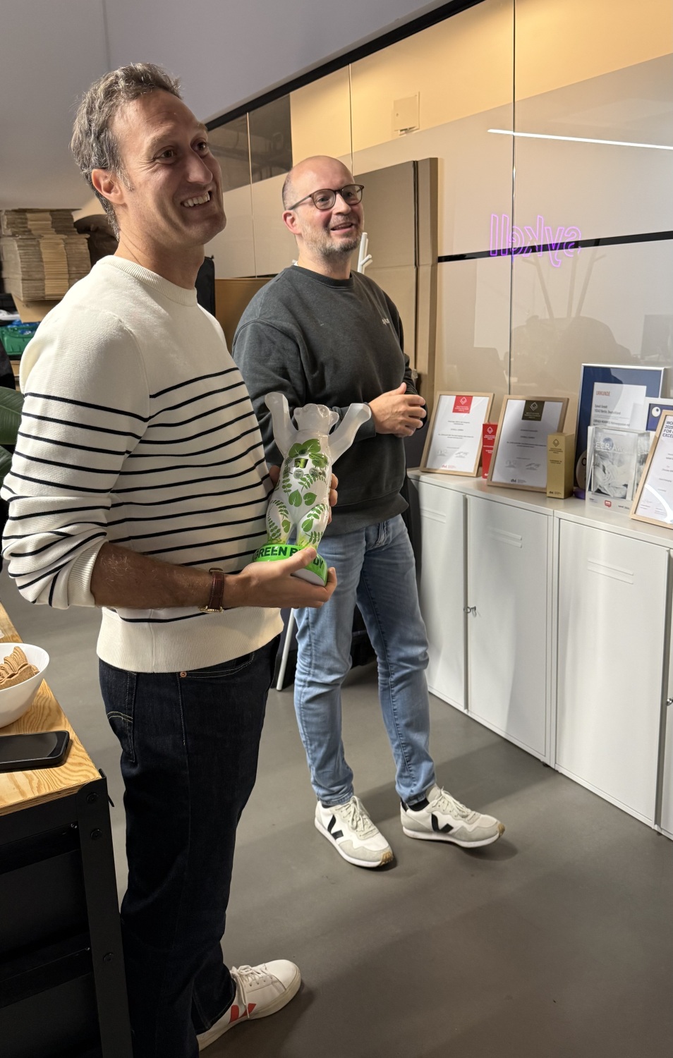 Zwei Männer stehen in einem Büro und lächeln, einer von ihnen hält den Green Buddy Award in den Händen