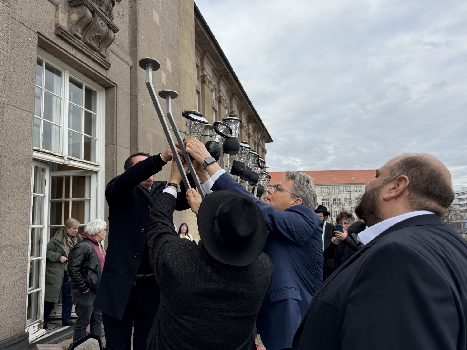Stellvertretender Bezirksbürgermeister Matthias Steuckardt, Rabbiner Yehuda Teichtal und Bezirksbürgermeister Jörn Oltmann entzünden den Leuchter draußen