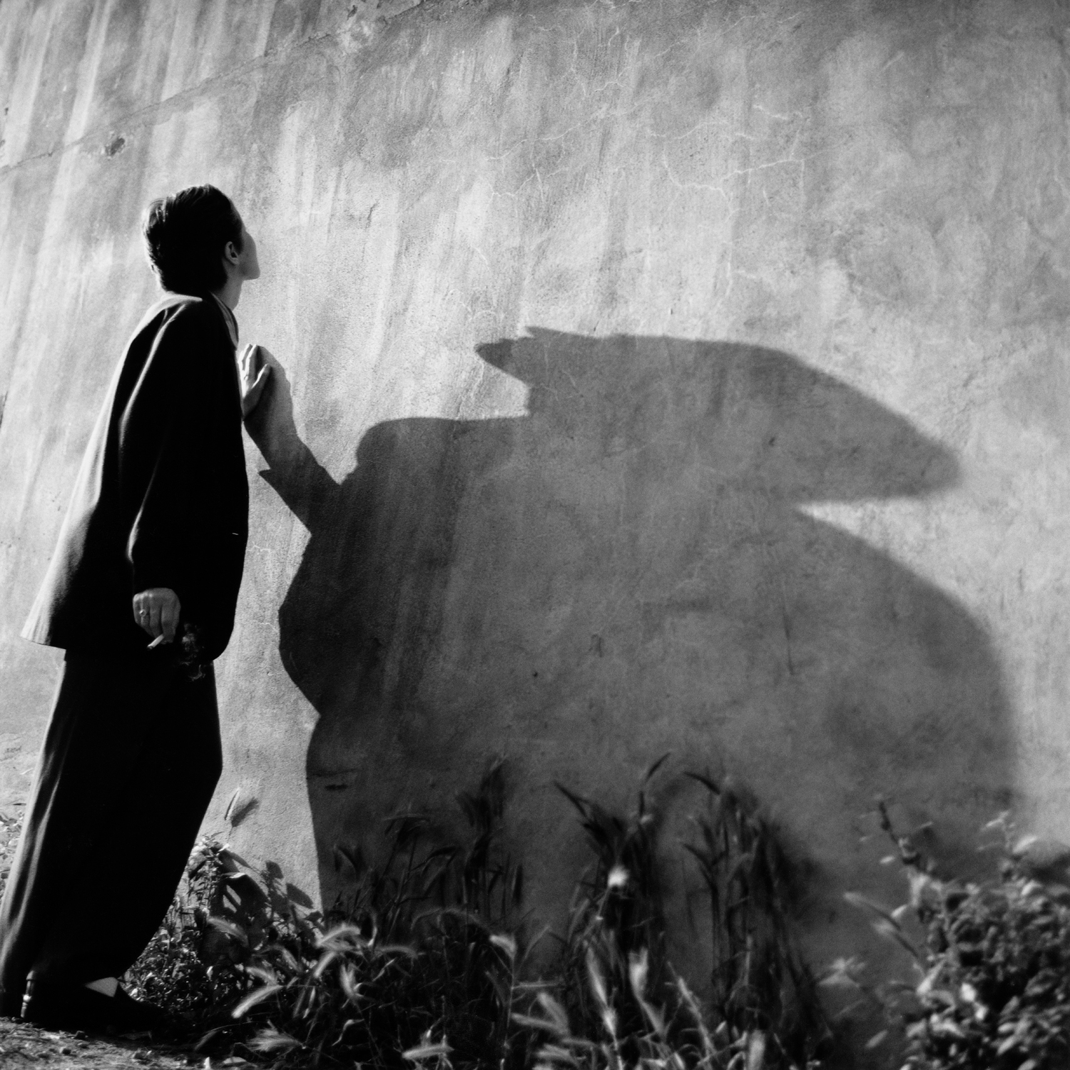 Schwarzweißfotografie; eine Person steht an einer Wand und berührt diese. Der Schatten der Person ist gut zu erkennen.