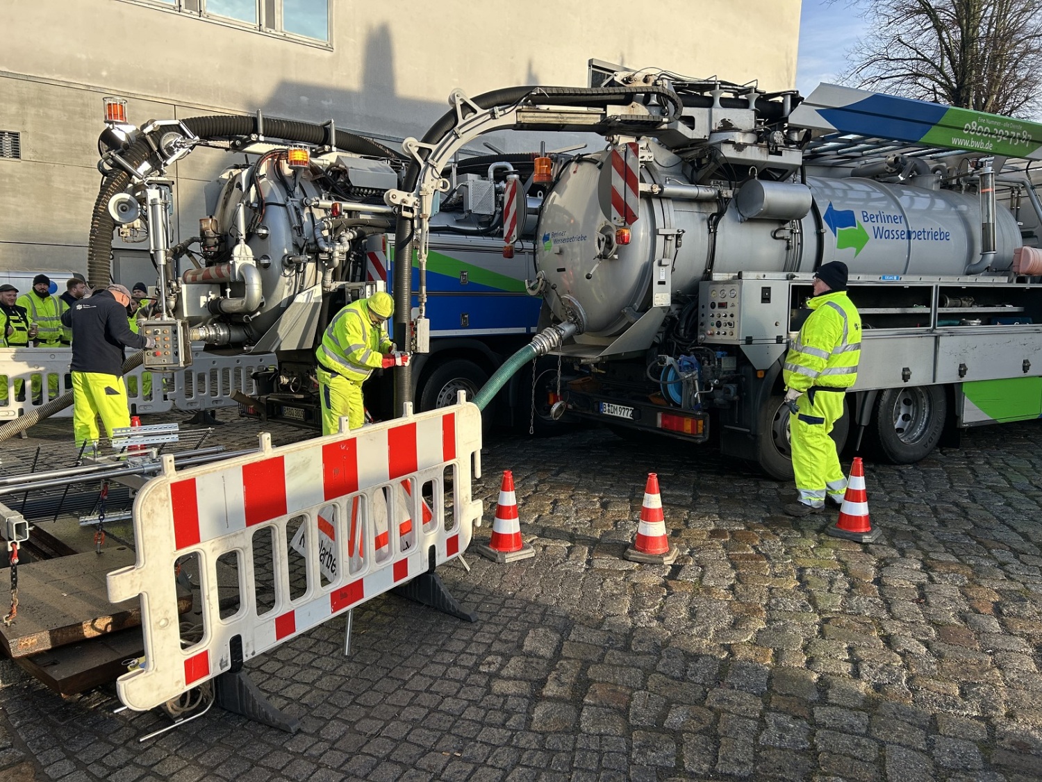 Zwei Wägen der Berliner Wasserbetriebe pumpen aus einem Gullyoch.