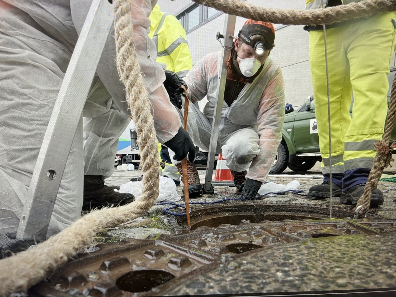 Personen mit Spezialausrüstung um einen Gully.