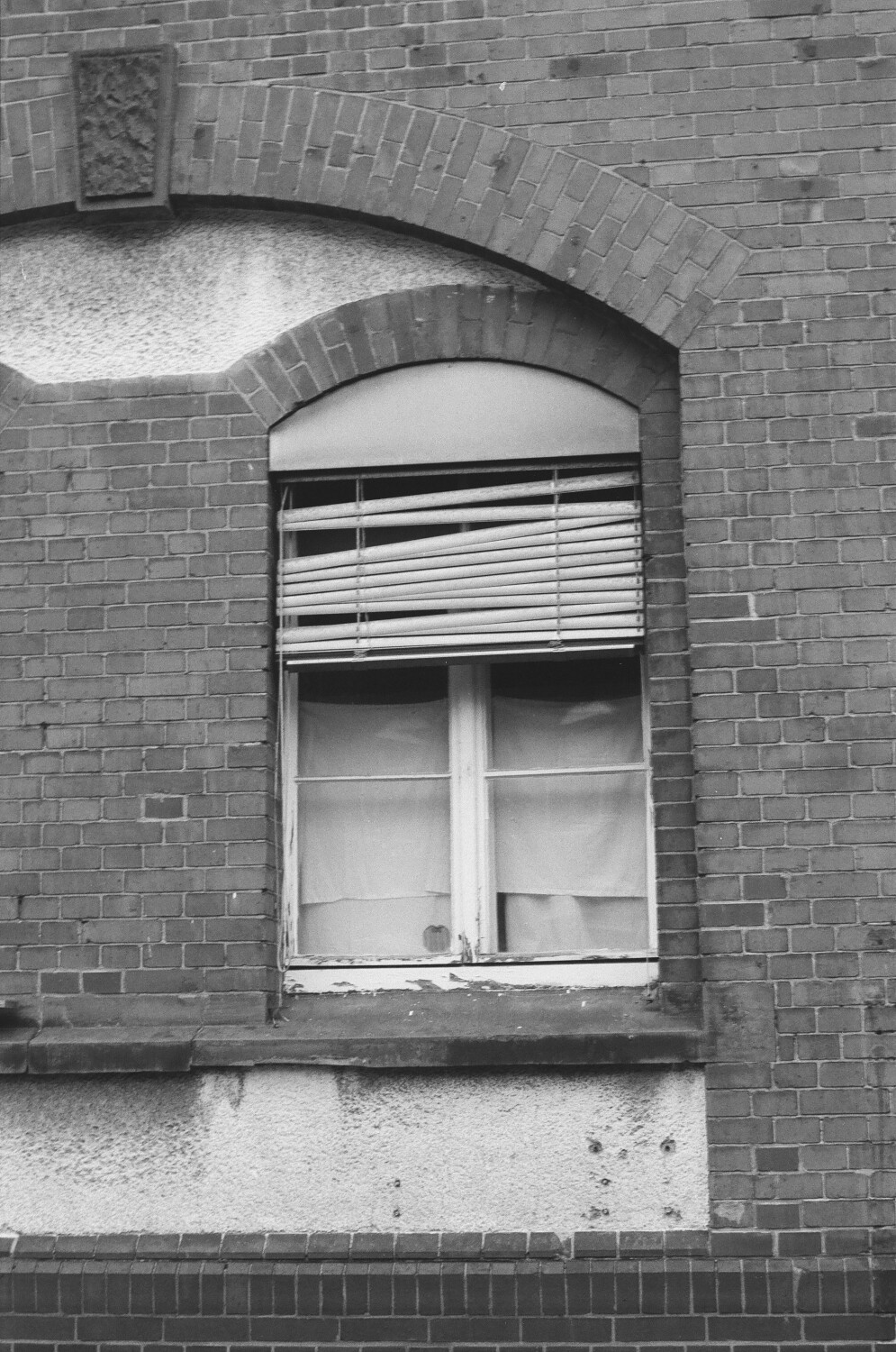 ein schwarz-weiß Foto von einer Hauswand mit einem Fenster mit kaputten Jalousien