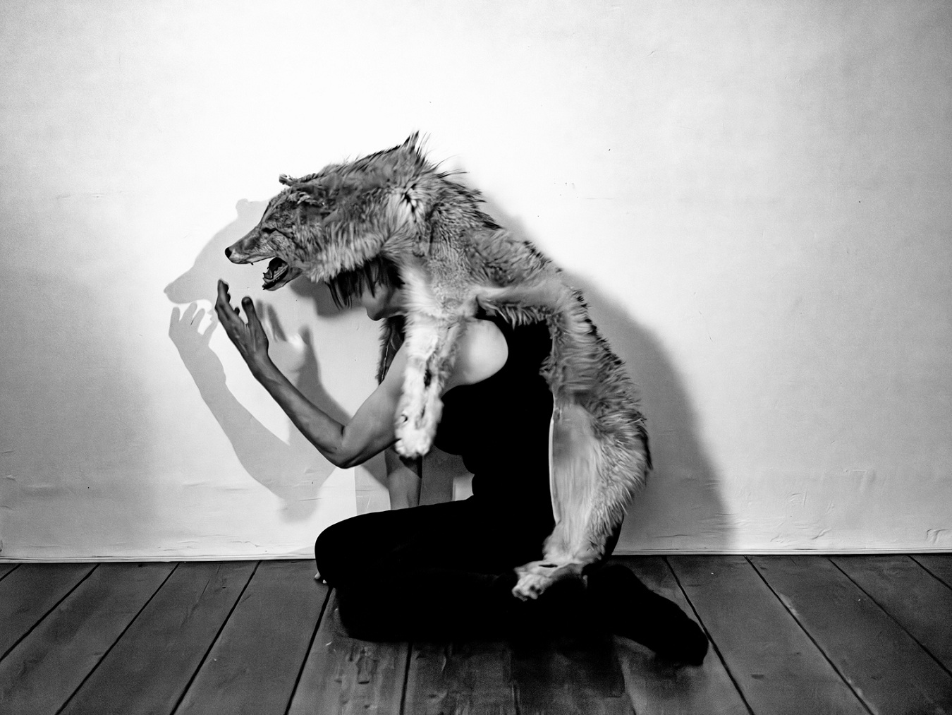 Schwarzweißfotografie von einer Person, die den Pelz eines Wolfes trägt.